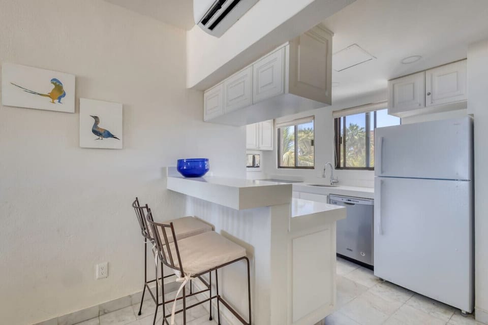 A fully-equipped kitchen featuring clean white countertops, a full-size refrigerator, an electric cooktop, and a stainless steel dishwasher.
