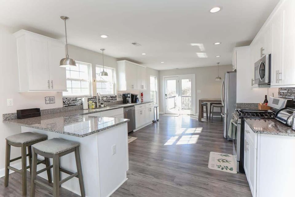 Kitchen with a kitchen island and bar stools, storage space, dishwasher, coffee maker, air fryer, table with additional seating, refrigerator, stove, oven, microwave, and toaster. Recessed lighting and access to a balcony. 