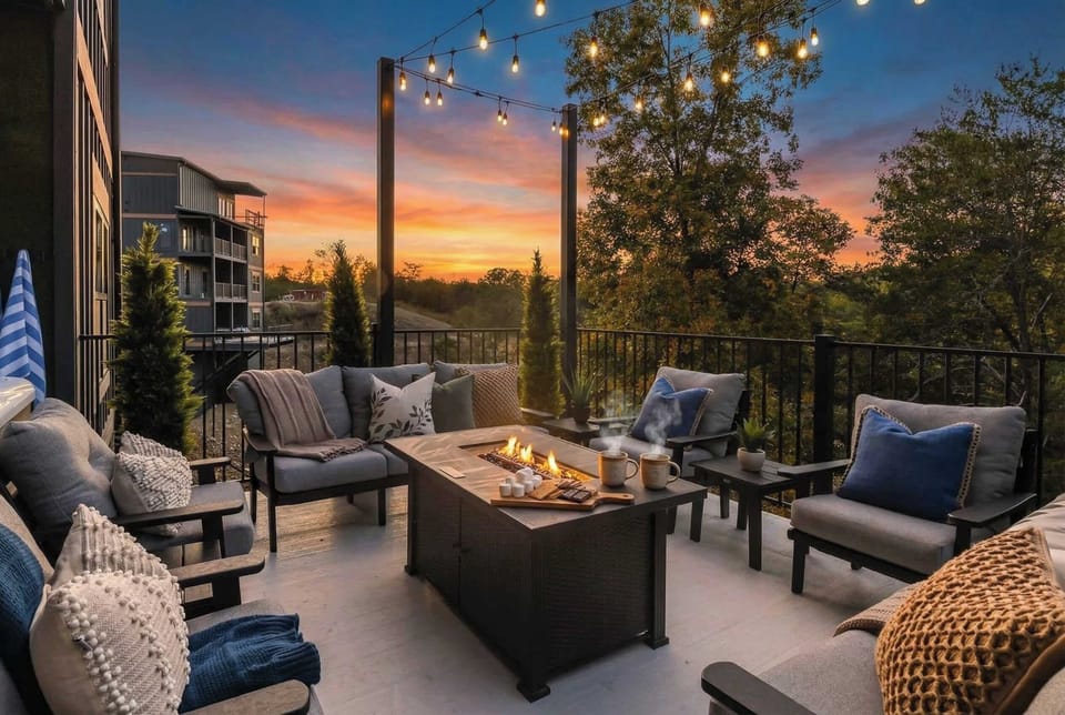 Cozy outdoor seating area with a fire pit and string lights overlooking a sunset view.