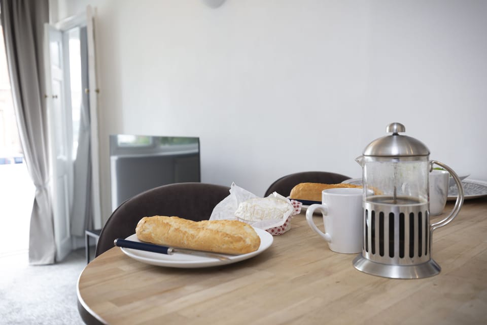 Wooden dining table with bread, coffee press, and mugs.