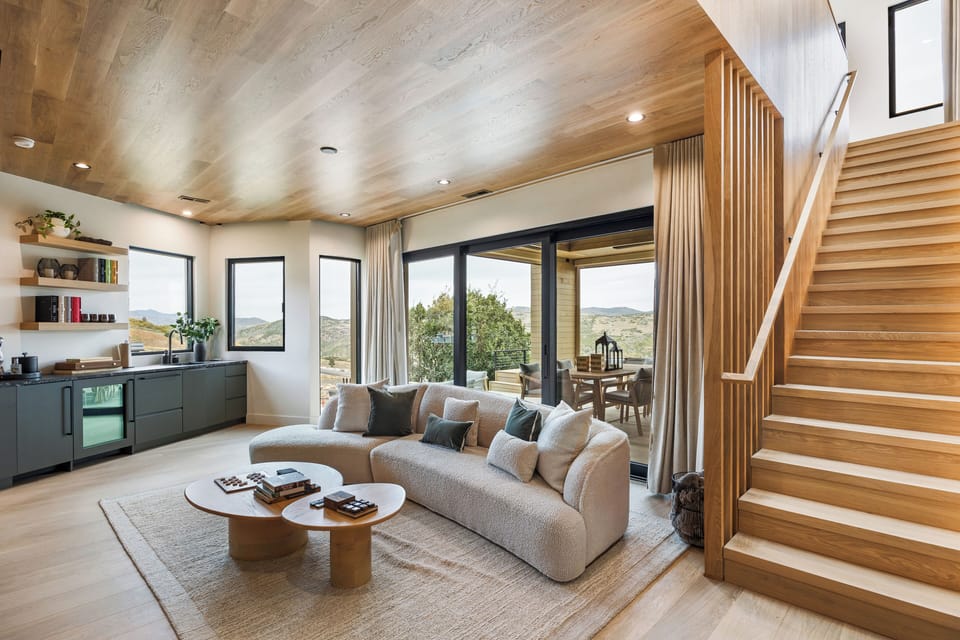 Bright and open living room featuring floor-to-ceiling windows, natural wood finishes, and seamless indoor-outdoor flow. A welcoming space designed for gathering and connection.