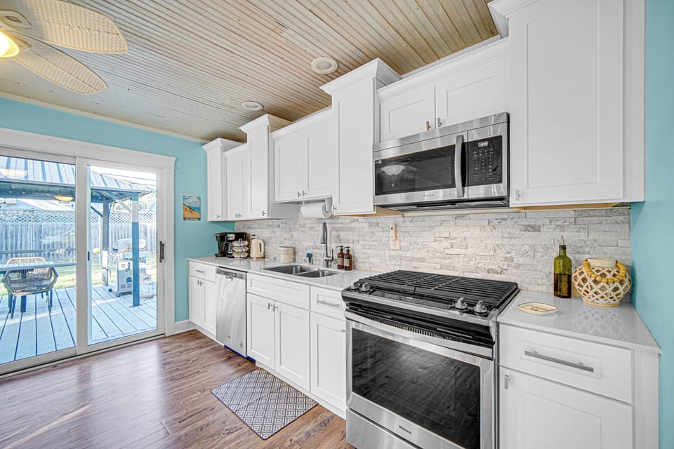 Fully stocked modern kitchen with stainless steel appliances, stone countertops, breakfast bar, and Keurig - everything you need for a beach getaway.