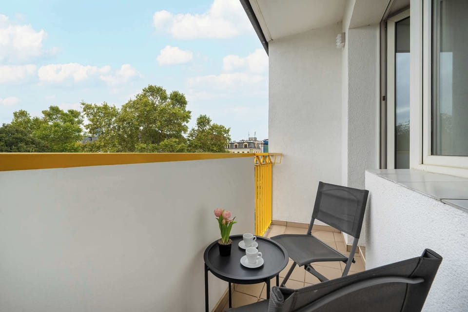 Another balcony angle showing two black chairs, a small table, and blue sky views.
