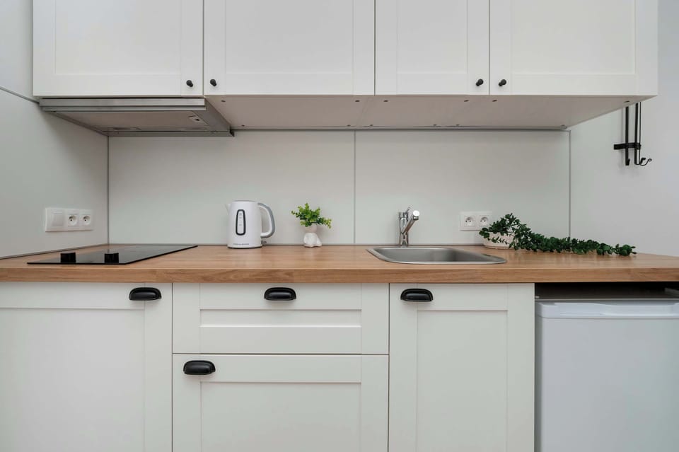 Another view of the kitchen with a focus on the white cabinets, light wooden countertops, and built-in stove. It’s a sleek, modern kitchen with a minimalist design.