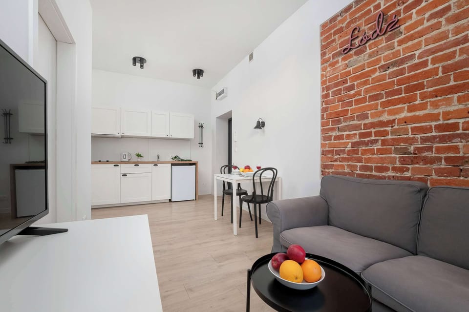 A wide shot of the living room, showcasing the brick wall, sofa, and a TV mounted on a white stand. The room is well-lit and spacious, with a minimalist and modern design.