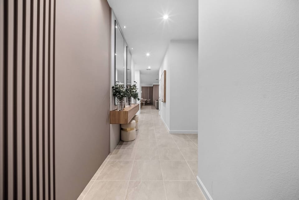 Welcome to a stylish entryway featuring light-colored tiles and warm wall tones that create a friendly atmosphere. The subtle greenery and wooden console add a natural touch, enhancing the modern aesthetic for your enjoyment.