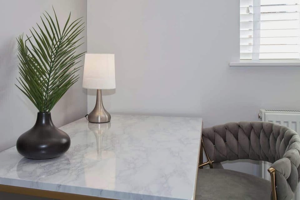 Cozy corner with marble-top table, green armchair, table lamp, and window with shutters.