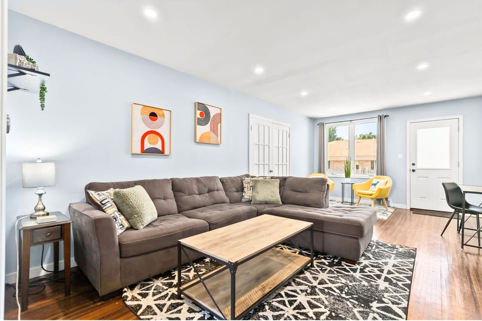 Living room with sectional couch, smart TV, desk area, additional seating area area by large front bay window.