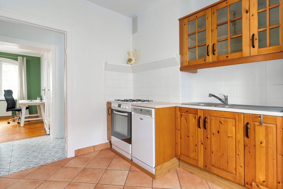 A kitchen with wooden cabinets and tiled floor. The space is well-lit and equipped with an oven and stove.