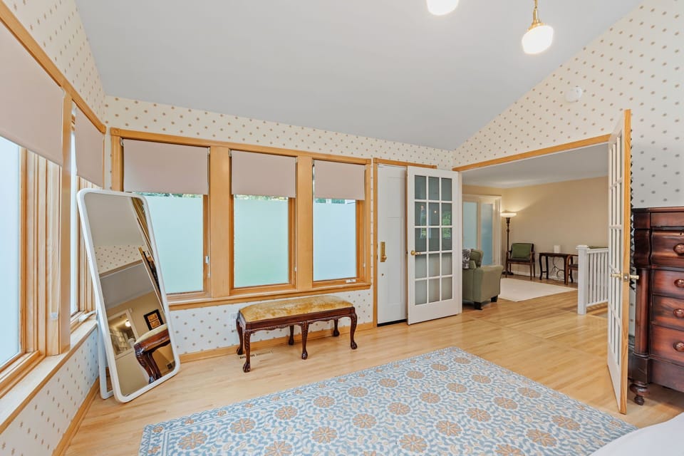 Your bright bedroom flows seamlessly into a cozy sitting area, featuring polished hardwood floors and charming patterned wallpaper that creates a welcoming retreat.