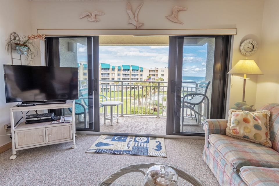 Relax in this cozy beachfront living room featuring ocean views, coastal décor, and direct balcony access—perfect for enjoying sunrise coffee or evening ocean breezes during your beach stay.