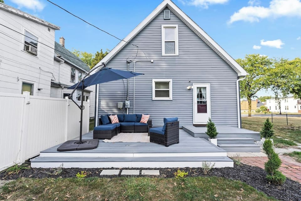 Charming backyard deck with cozy sectional seating and a large umbrella, perfect for morning coffee, evening chats, or relaxing outdoors during your stay.