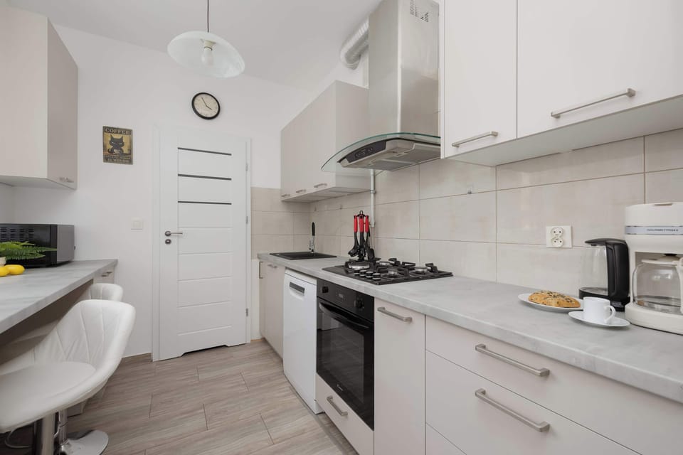 A modern white kitchen with a stove, cabinets, and small dining counter. Functional and clean, it balances simplicity with warmth.