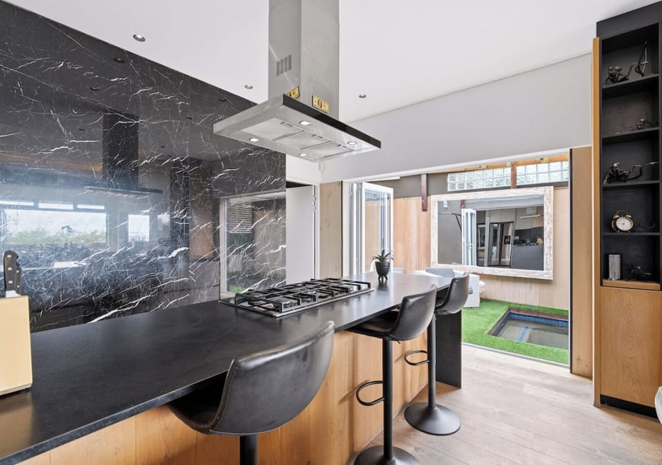 Sleek kitchen with cooktop island, bar stools and sunlit courtyard access