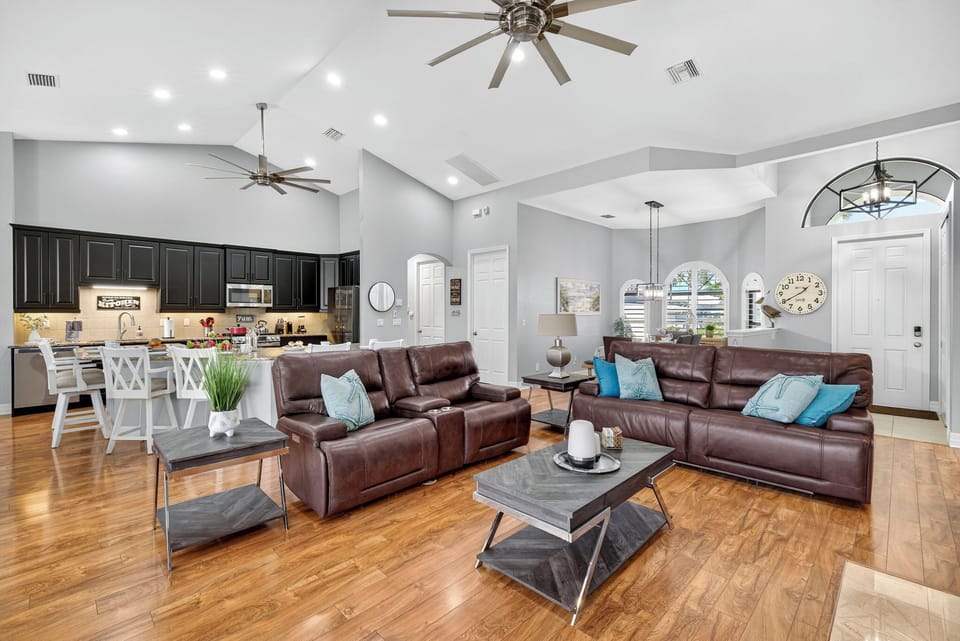 Open-concept living area featuring cozy leather seating, a sleek fireplace, and sliding glass doors leading to the pool and outdoor dining area — perfect for relaxing or entertaining.