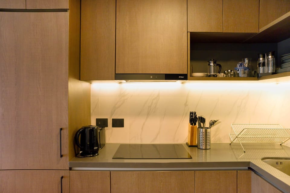 Sleek and modern kitchen with all essentials for a comfortable stay, featuring stylish wooden cabinets and ambient lighting.
