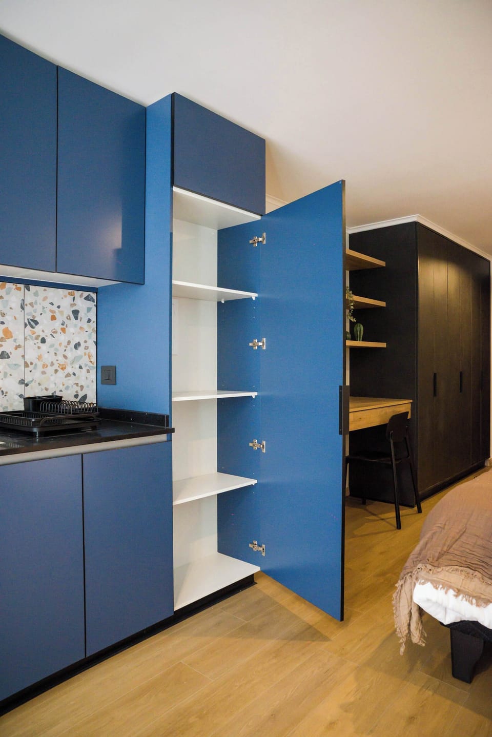 Chic studio kitchen with vibrant blue cabinets and terrazzo backsplash, perfect for a stylish and functional stay.