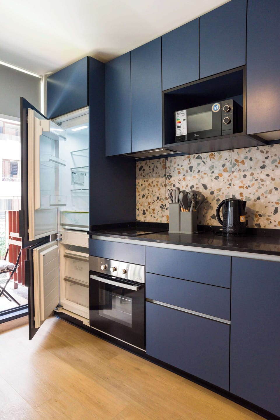 Sleek kitchen with blue cabinets and terrazzo backsplash, perfect for culinary adventures in your cozy studio.