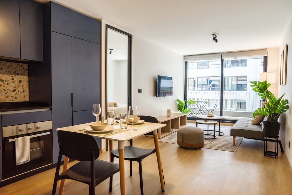 Chic studio with modern kitchen, cozy seating, and expansive windows offering vibrant city views. Ideal for a serene urban retreat.