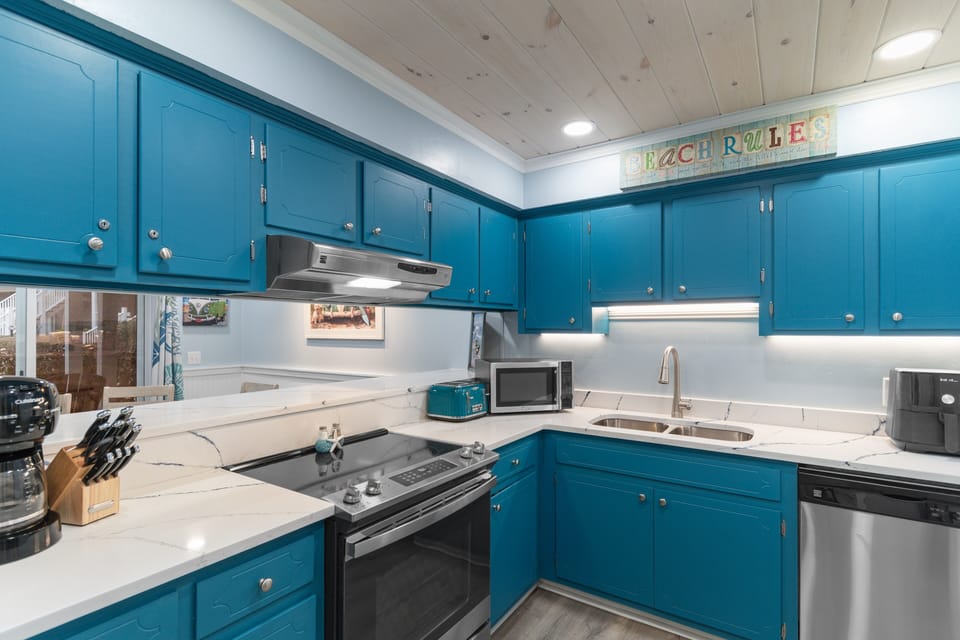 Cook with joy in your bright, fully-equipped kitchen featuring vibrant turquoise cabinets and modern stainless steel appliances.