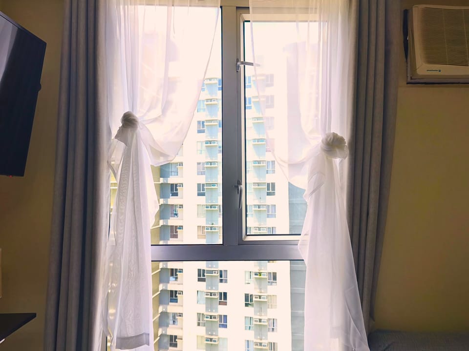 Bright window with city view & soft curtains creates a calm, relaxing vibe.