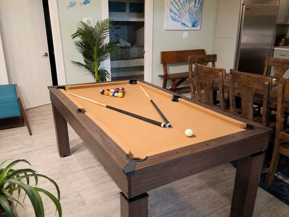 Pool Table: Versatile Infinity game table set up for billiards, featuring a smooth tan playing surface, full set of pool balls, cue sticks, and sturdy wood-frame design for indoor entertainment.