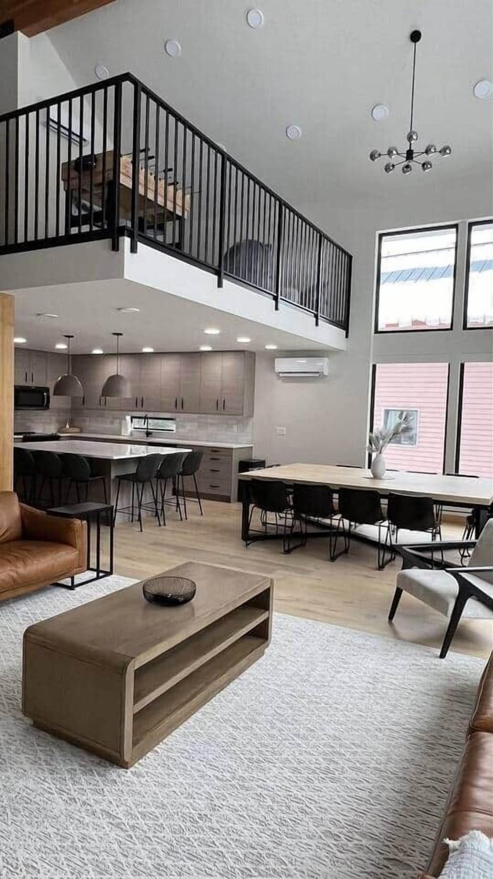 Experience the spacious great room: combining a modern kitchen with sleek cabinetry, a huge dining table for gatherings, and a cozy family room with plush leather sofas. Large windows and a stylish loft overlook the warm wooden floors. 