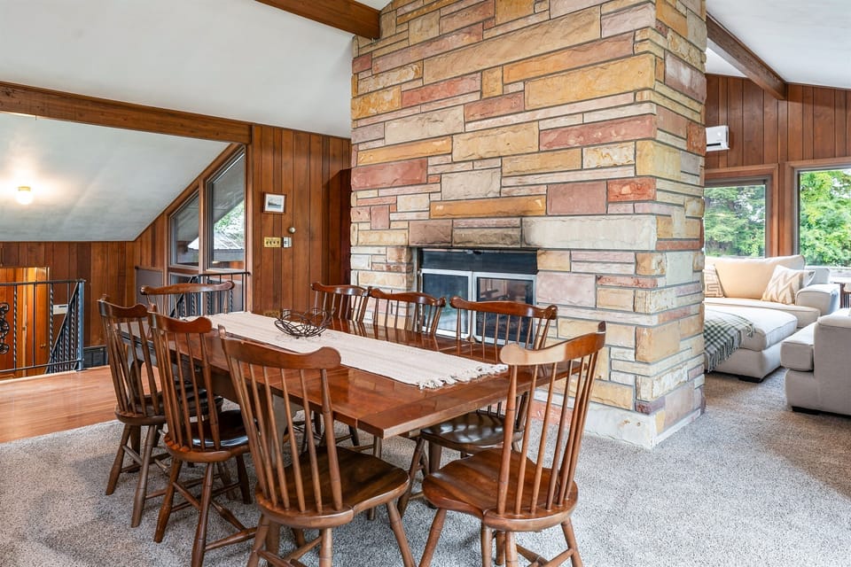 Enjoy cozy dinners by the stunning stone fireplace in this open-concept dining space, blending rustic charm with modern comfort.