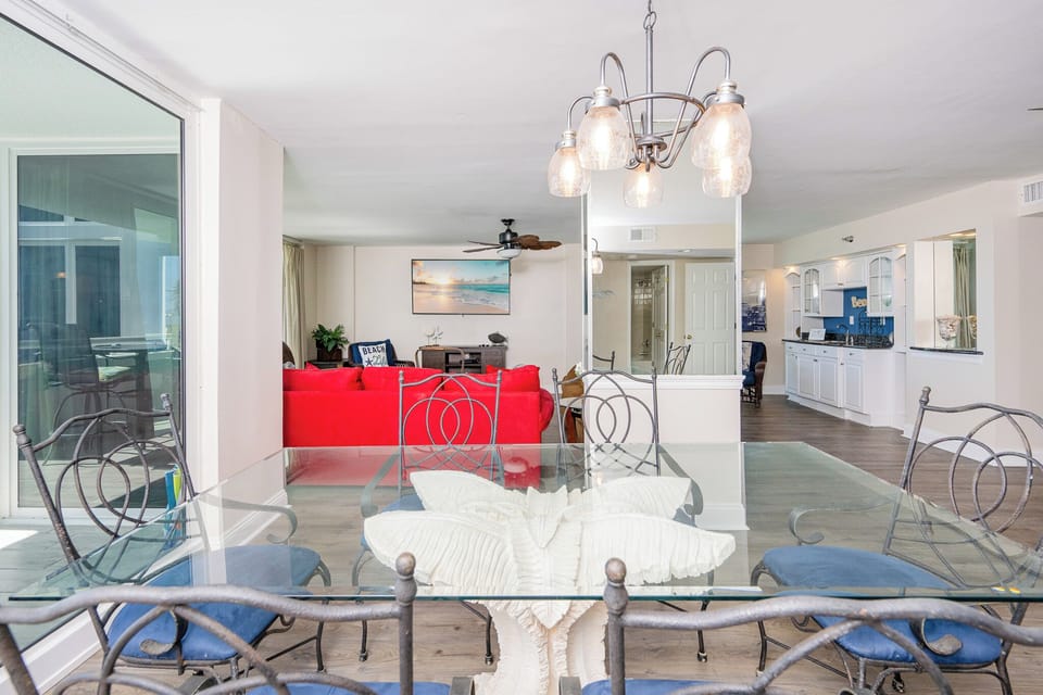 Dining area features a glass table with decorative accents and a cozy living space in the background, inviting relaxation