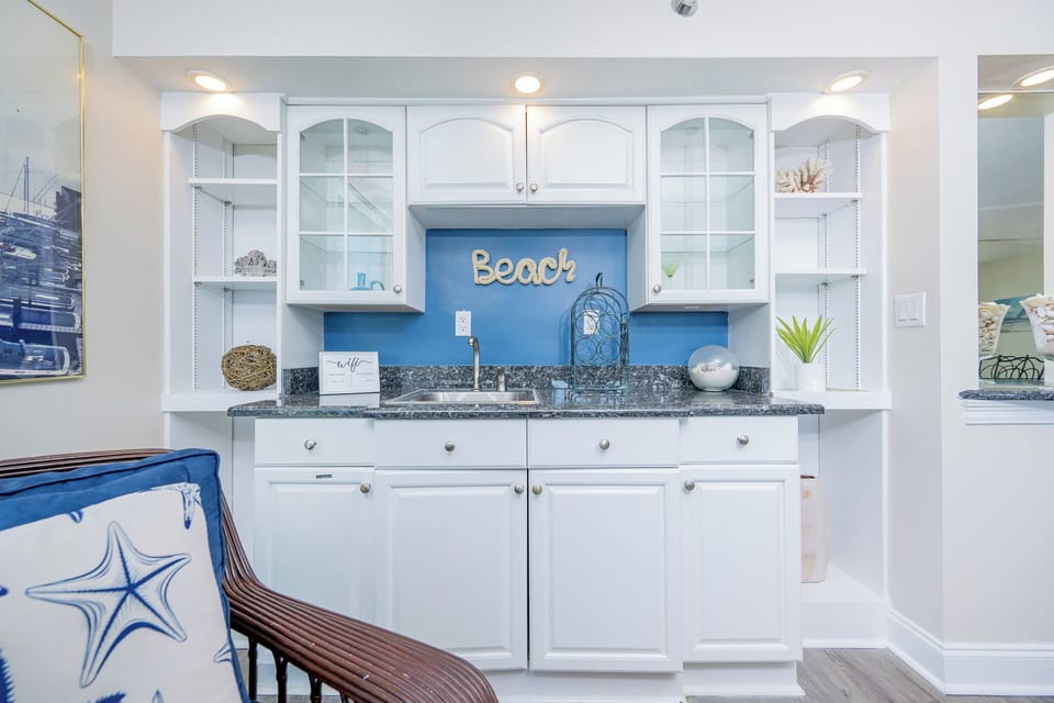 Stylish wet bar area featuring white cabinetry, granite countertops, and beach-themed decor for a coastal vibe