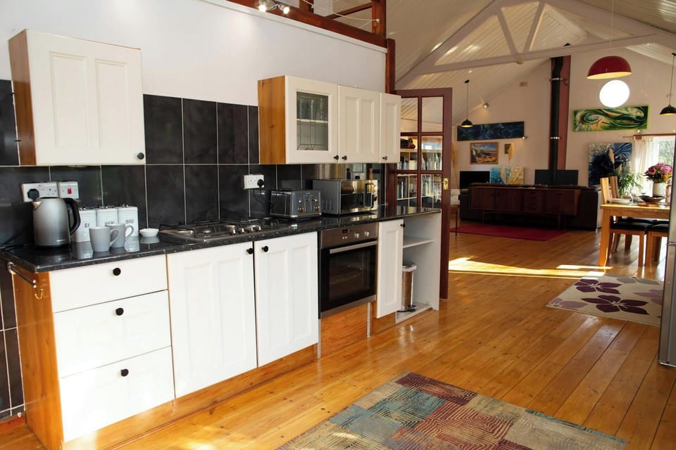 Open-plan kitchen with white cabinets, black worktop, and wooden floor