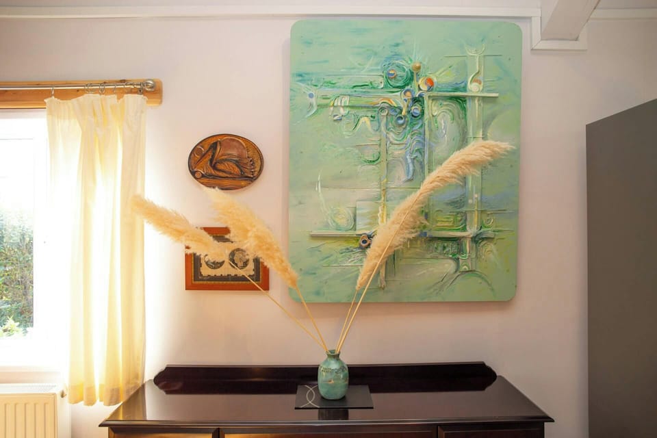 Dark wooden sideboard with a turquoise vase holding pampas grass, under abstract artwork