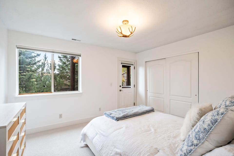 A serene guest room with a plush queen bed and large windows overlooking the surrounding pines.