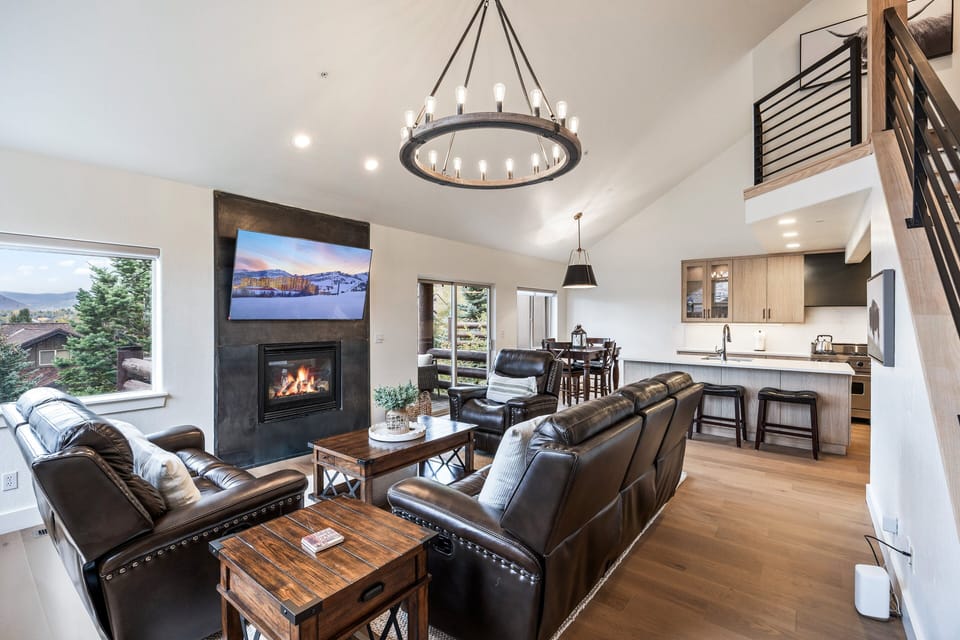 A stunning open-concept living area featuring vaulted ceilings, a modern chandelier, and a sleek gas fireplace.