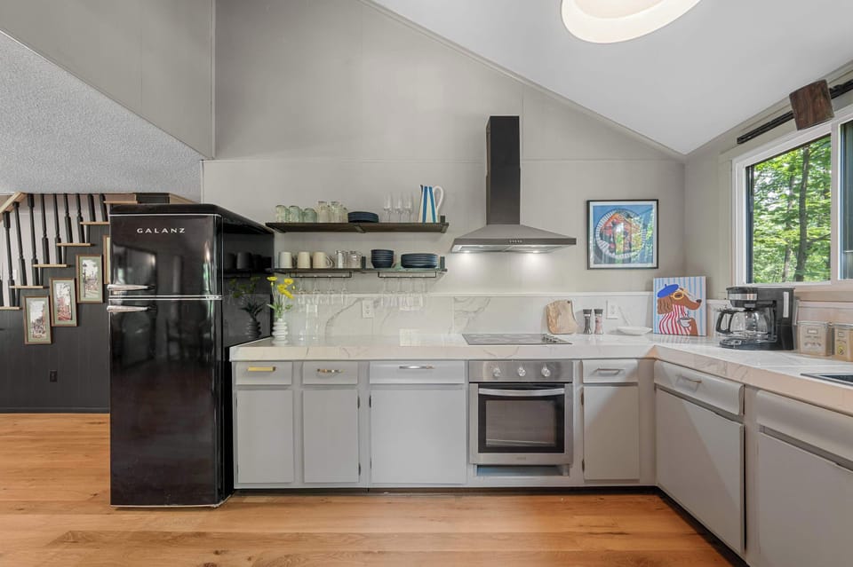 The beautifully updated kitchen blends modern style with functionality, featuring sleek appliances, open shelving, a dishwasher, oven and range, microwave, and coffee maker.