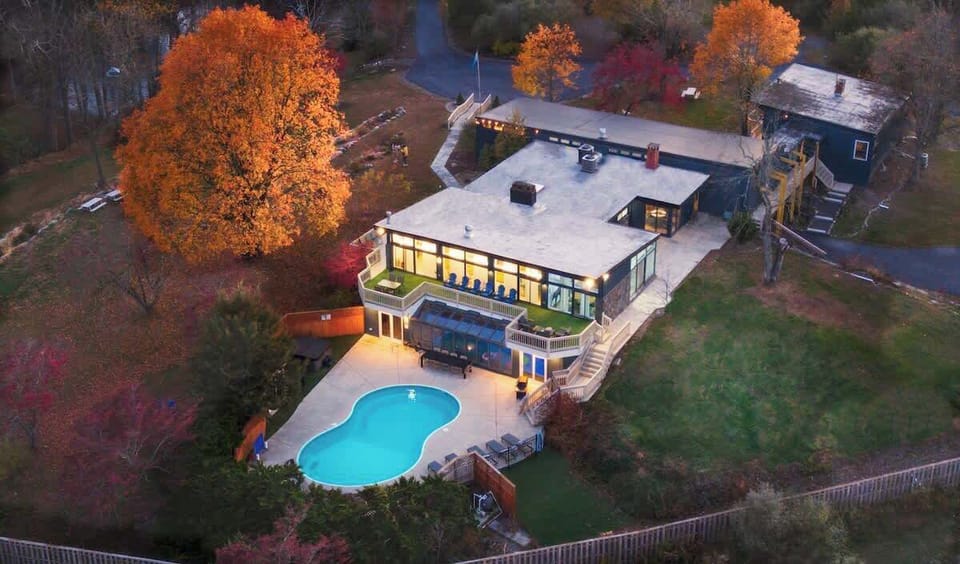 Aerial view of the striking modern home surrounded by trees, showing the pool & spacious grounds.