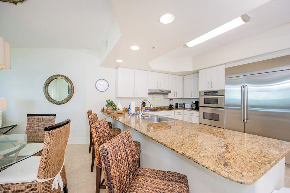 Modern kitchen featuring granite countertops, modern stainless appliances, and stylish woven bar stools for casual dining