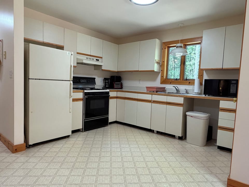 Your fully equipped kitchen awaits—prepare home-cooked meals with a full-size fridge, stove, oven, microwave, and coffee maker, all surrounded by peaceful woodland views through the window.