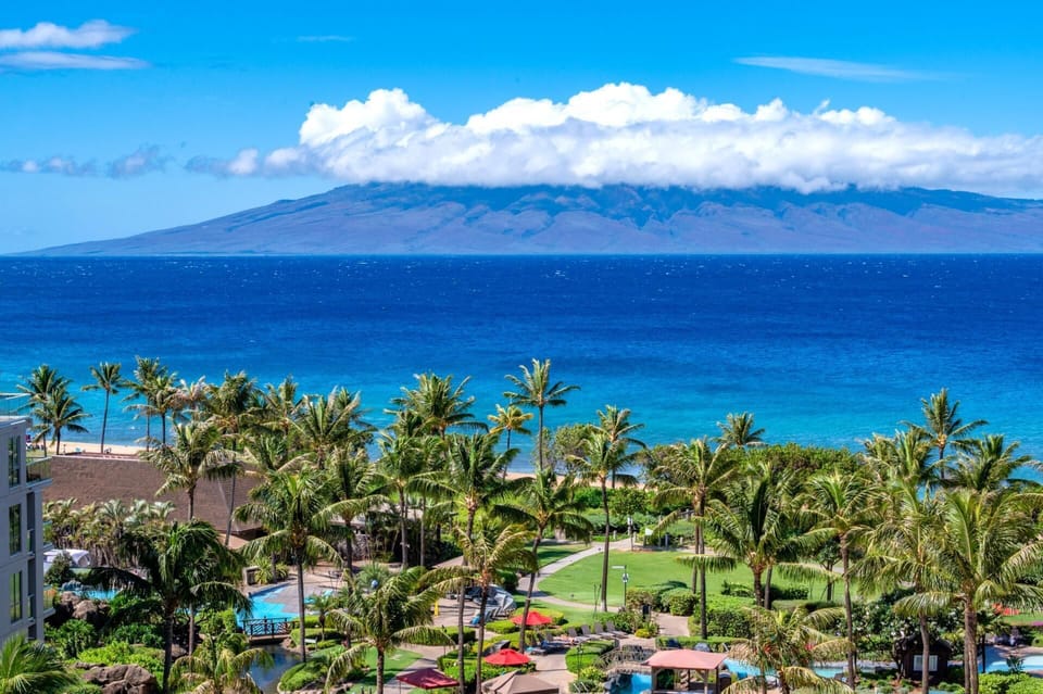 Panoramic ocean views to Molokai rise beyond the turquoise shoreline, with Honua Kai tropical pools, palms, and gardens creating a postcard-perfect foreground. HKK-829