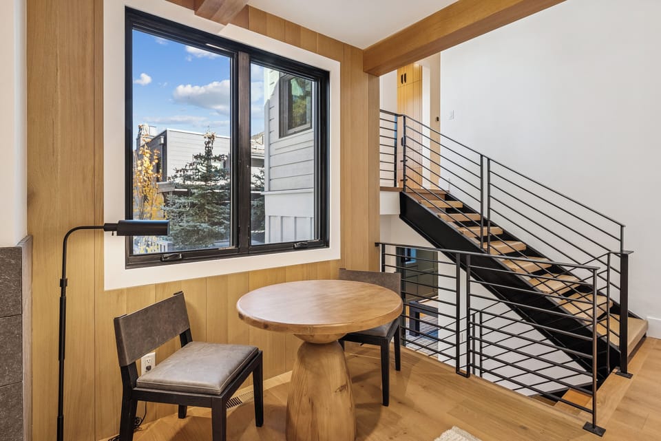 Compact sitting corner with round table beside staircase and floor-to-ceiling windows.