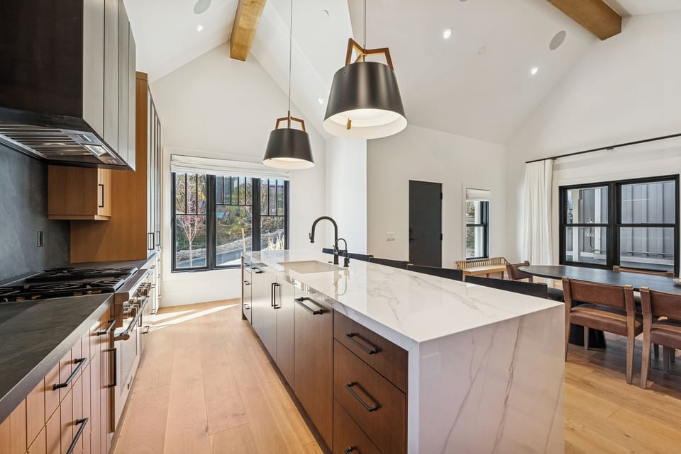 Bright modern kitchen with waterfall island, wood cabinetry, and vaulted ceiling.