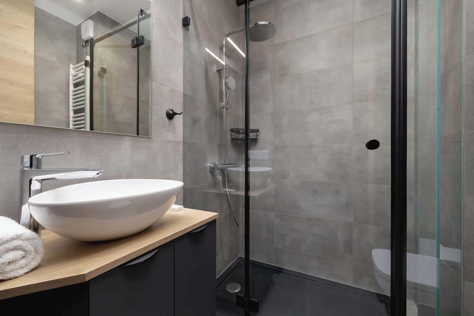 A minimalist bathroom with a white sink, a mirror, and grey tiled walls.