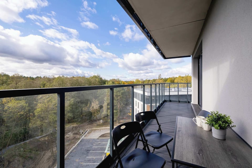 A wide shot of a balcony with a scenic view, showing a glass railing and lush greenery.