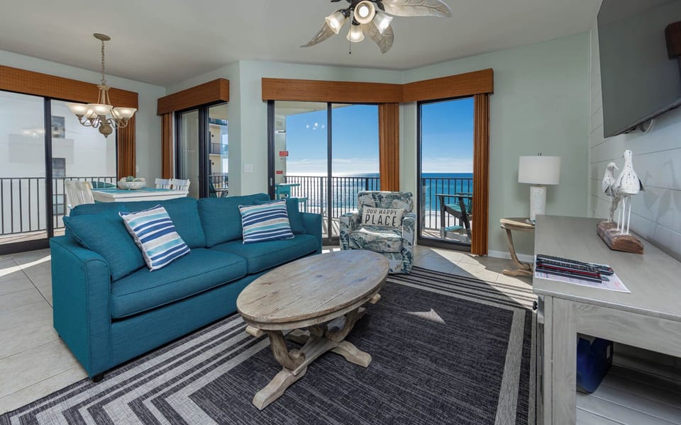 Living area features a teal sofa with queen sleeper, a wooden coffee table, and stunning gulf views