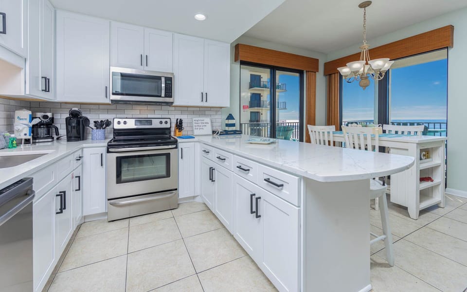 Bright kitchen features white cabinetry, spacious countertop, coffee corner, and a dining area with gulf views