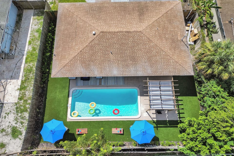 Aerial view of backyard with pool, lounge chairs, umbrellas, and shaded dining.
