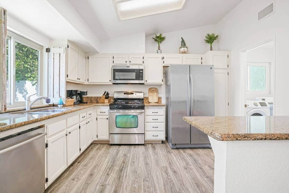 Fully stocked kitchen has stainless steel appliances and 3 coffee makers: A Keurig, a standard drip coffee maker, and a French press. It also has plates, cups, utensils, chef's knives, pots, pans, blender, and electric kettle, wine glasses, etc.