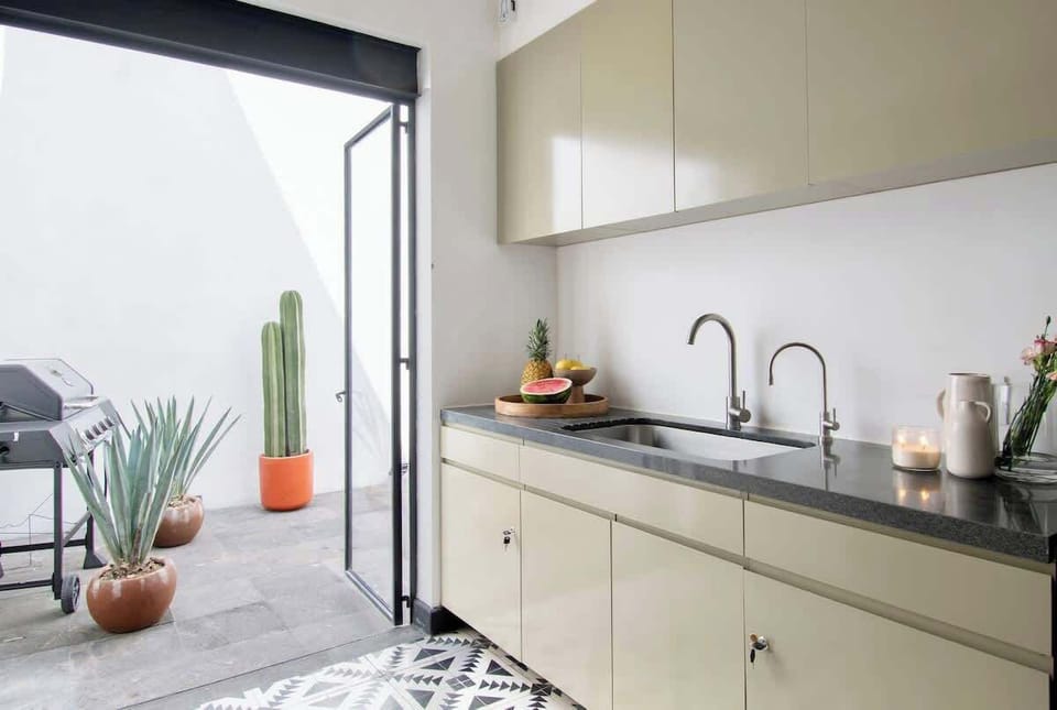 The kitchen opens directly onto a serene patio, blending indoor elegance with outdoor charm. Soft light, sleek cabinetry, and greenery beyond the glass create a harmonious space designed for both cooking and connection.