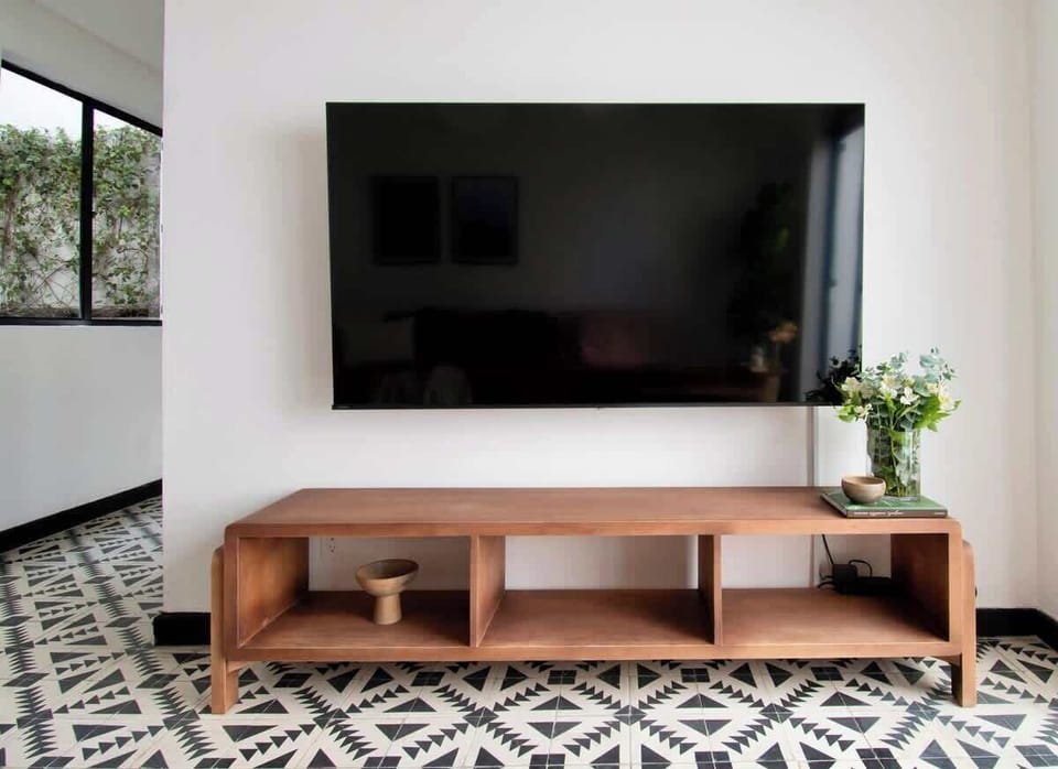 A sleek wooden console and large smart TV anchor the living area with minimalist elegance. Clean lines and subtle greenery keep the design balanced between modern comfort and visual warmth.