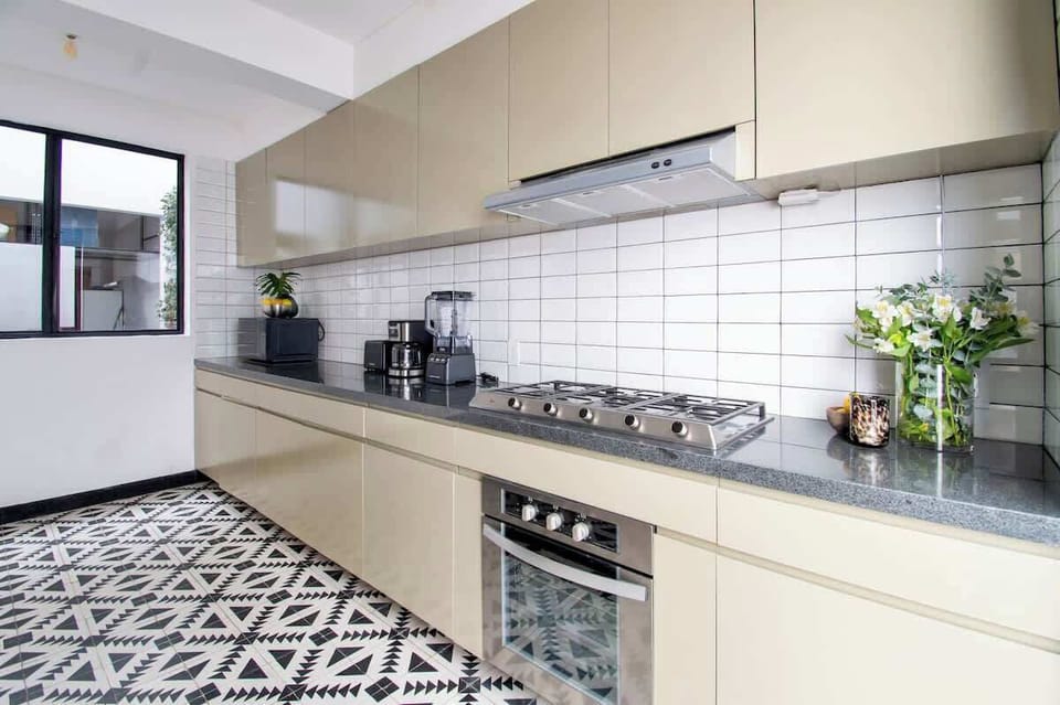 A sleek, fully equipped kitchen with modern appliances, minimalist olive cabinetry, and a clean tiled backsplash. Thoughtful design and natural light make it as functional as it is visually striking